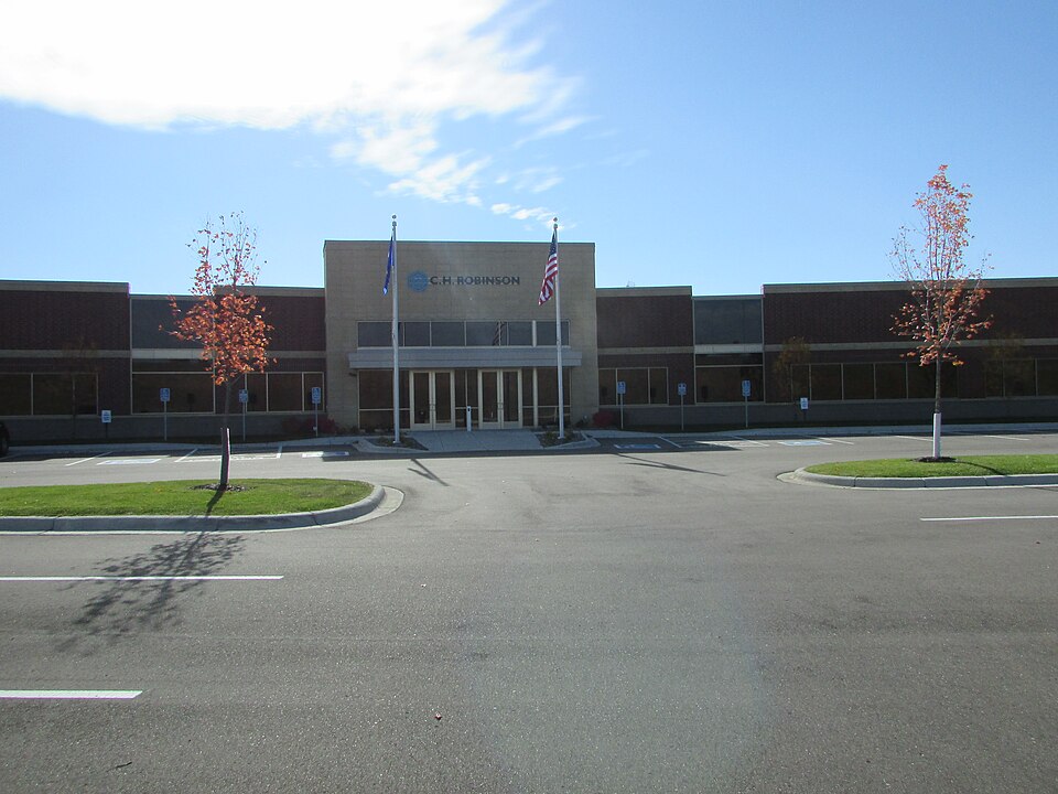 C.H. Robinson's IT building in Eden Prairie, Minnesota, in October 2014: a low brick and stone office block with the company's name above a glass entrance, two flagpoles in front and young trees in fa