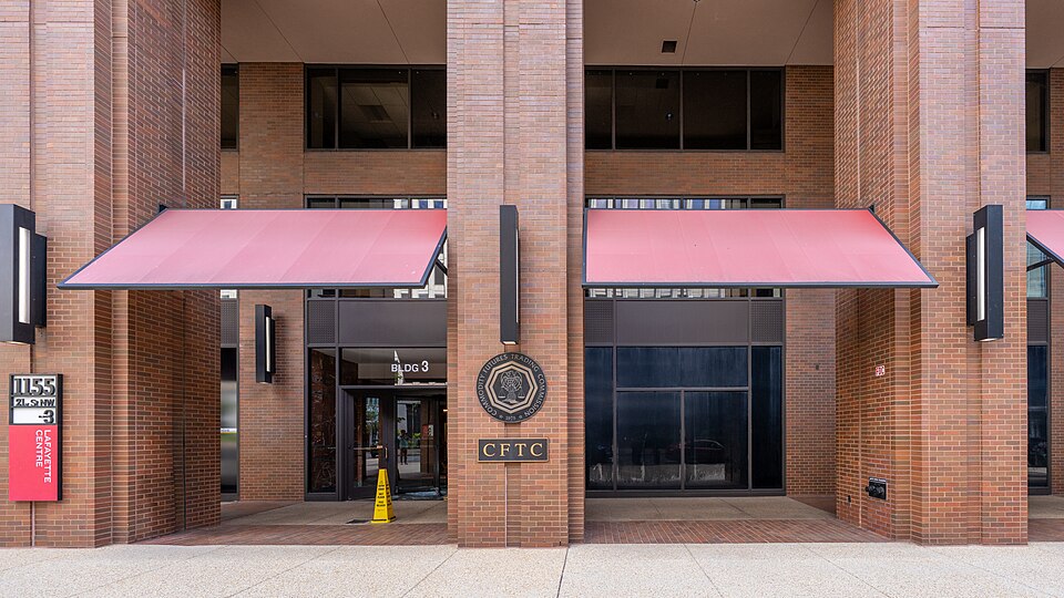 The entrance to the Commodity Futures Trading Commission's headquarters at Three Lafayette Centre, 1155 21st Street NW in Washington, with the agency's seal and a CFTC plaque on a brick pillar between
