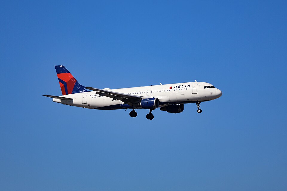 A Delta Air Lines Airbus A320 in white, red and blue livery, landing gear down, on approach to Atlanta's Hartsfield-Jackson airport under a clear blue sky