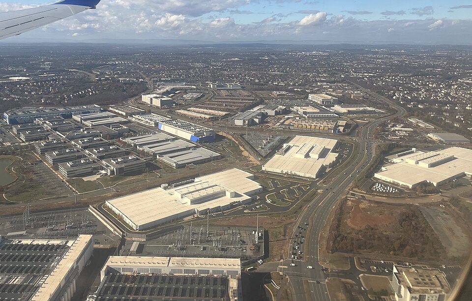 Aerial view of large data center buildings near Ashburn in Loudoun County, Virginia, with two electrical substations between them and rows of rooftop equipment in the foreground, seen from an aircraft