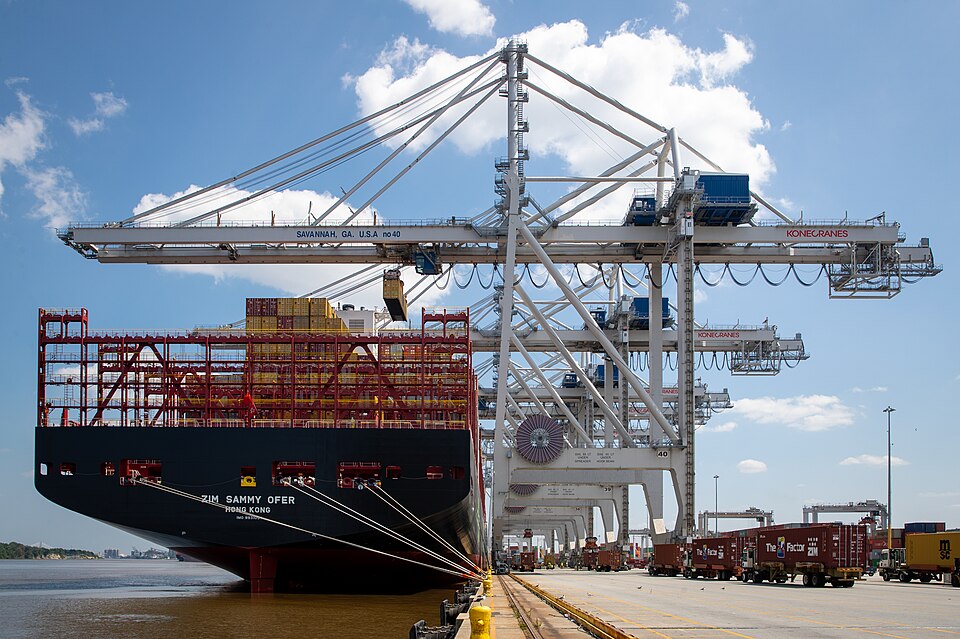 The container ship ZIM Sammy Ofer moored under ship-to-shore cranes at the Port of Savannah, Georgia, with container trucks lined up on the quay, in June 2023