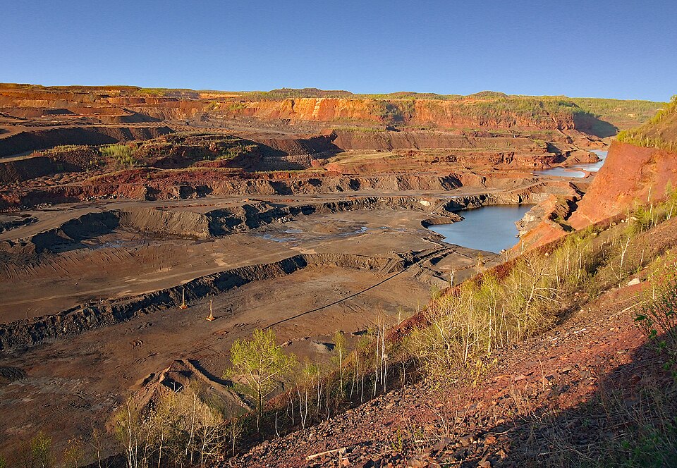 The Hull-Rust-Mahoning open-pit iron mine at Hibbing, Minnesota, on the Mesabi Iron Range, seen from the mine overlook in May 2014: red, terraced pit walls, a pit lake and young trees
