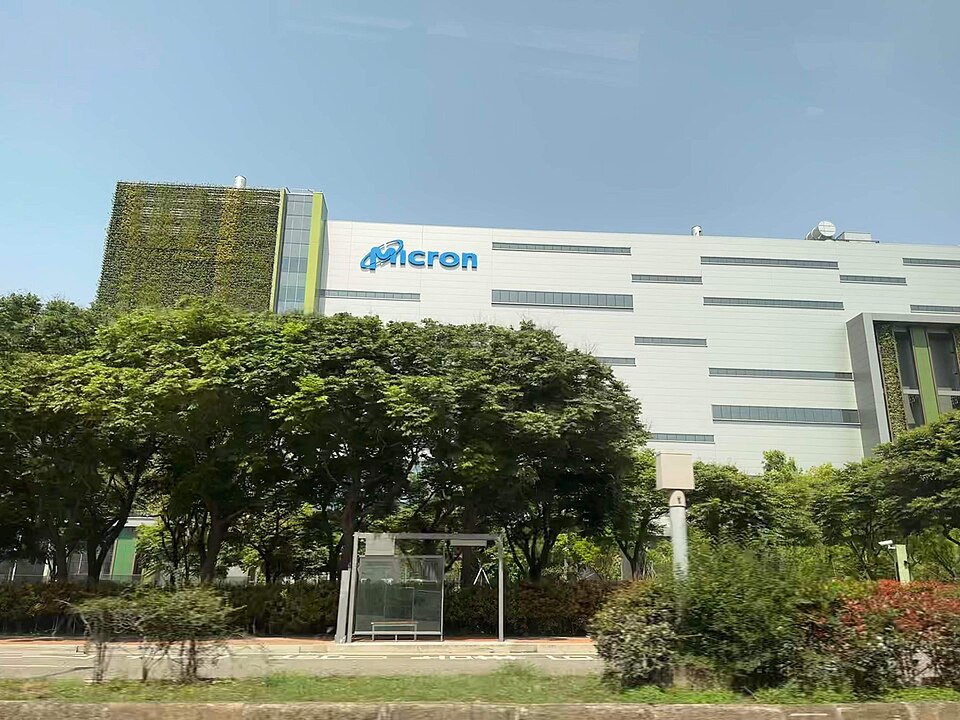 A white Micron memory plant with the company's blue name on its wall, seen across a line of trees in Taichung, Taiwan, in 2023
