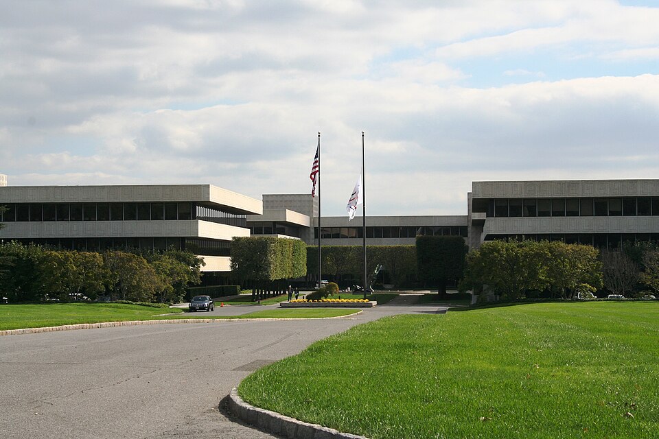 PepsiCo's headquarters in Purchase, New York: low concrete office buildings behind a lawn and a curving driveway, with two flagpoles at the entrance