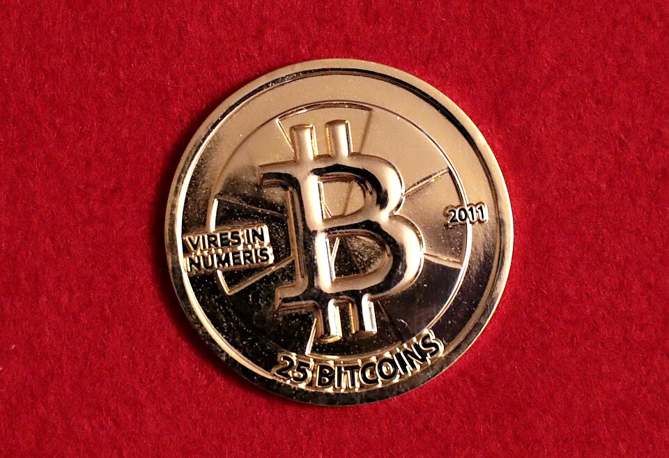 A gold-coloured Casascius physical bitcoin from 2011, stamped 25 bitcoins, lying on red felt