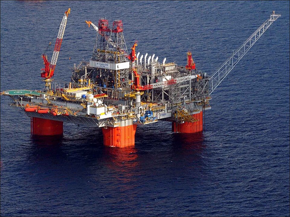 BP's Thunder Horse semisubmersible production platform in the Gulf, seen from the air: a deck of cranes, a drilling derrick and process equipment on four orange columns standing in dark blue water