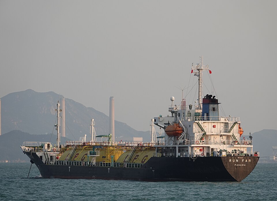 A small liquefied petroleum gas carrier, the Run Far, its deck lined with yellow pressure tanks lettered LPG, in calm water off Peng Chau, Hong Kong, with hills and two tall chimneys behind it under a