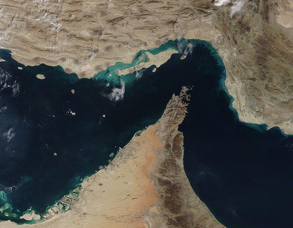A satellite view of the Strait of Hormuz: Iran's coast across the top, the Musandam peninsula of Oman reaching north into the narrow water from the desert of the United Arab Emirates, the Persian Gulf