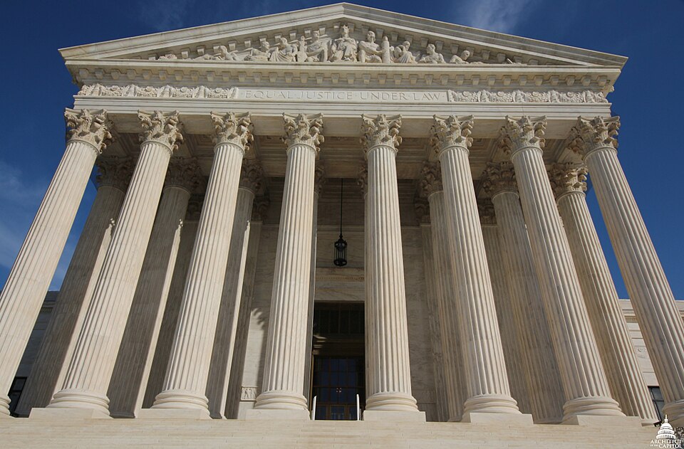 The west front of the Supreme Court Building in Washington seen from the foot of its steps: tall fluted marble columns with carved capitals hold up a pediment of sculpted figures above the words EQUAL